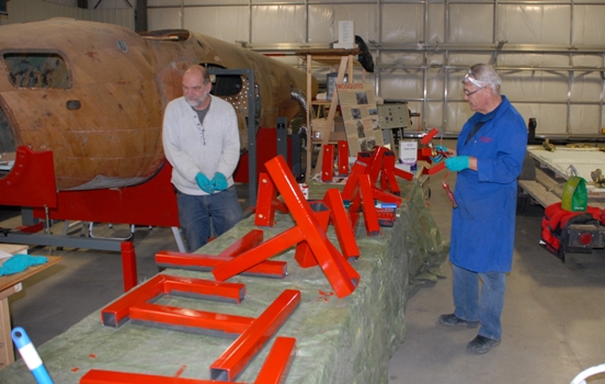 Steel angles and brackets being painted to match the fuselage fixture are painted and prepared by Jack McWilliam and Dick Snider for a new wing holding fixture.